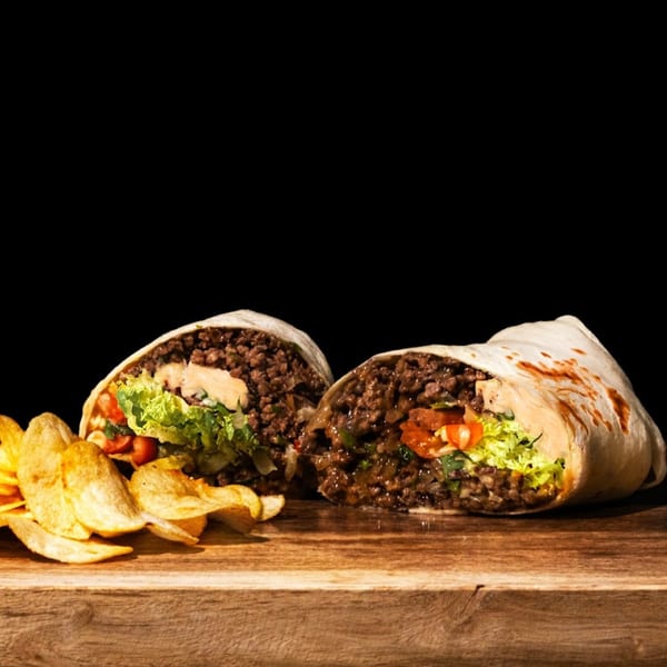 Two halves of a Munchies burrito, filled with ground meat, lettuce, and tomatoes, served with chips.